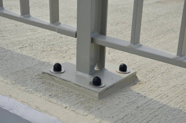 перила на мосту с вертикальными решетками ограждения, закрепленными на земле четырьмя бетонными винтами. пластиковые колпачки - Фото, изображение
