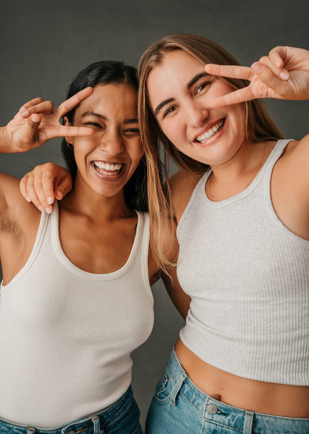 Two casual dressed females in there jeans and t shit making the piece symbol. High quality photo - Foto, Imagem