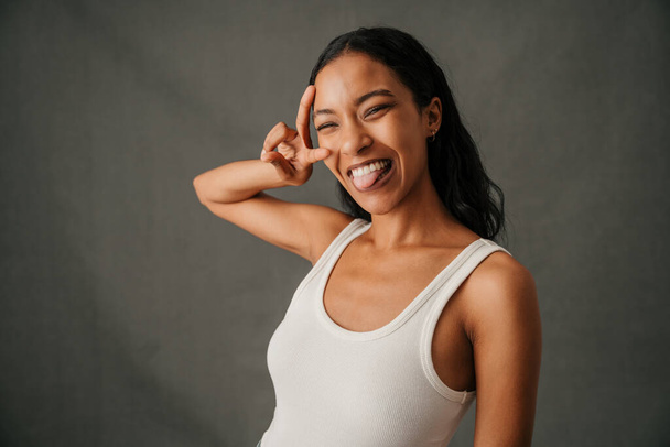 Stüdyoda, gündelik giysiler içinde, barış işaretini gülümserken gösteren çok ırklı bir kadının fotoğrafını çek. Yüksek kalite fotoğraf - Fotoğraf, Görsel