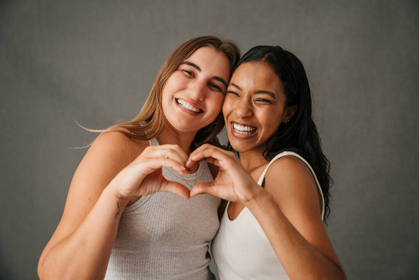 Two fun-loving laughing girlfriends making a heart sign with there hands. High quality photo - Fotó, kép