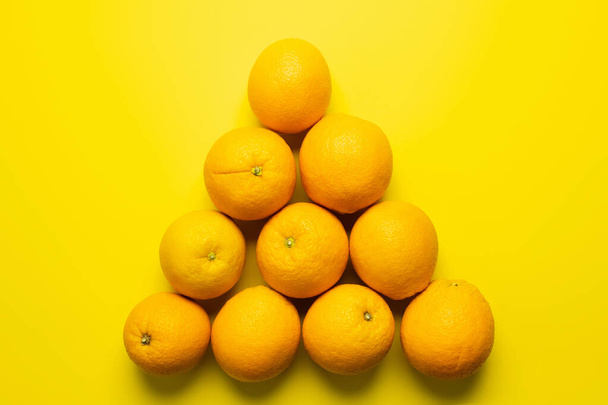 Flat lay with oranges in triangle shape on yellow background  - Photo, Image