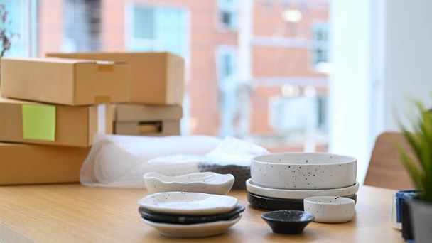 Set of ceramic products and parcel boxes on wooden table in modern home office. E-commerce, Online selling concept. - 写真・画像
