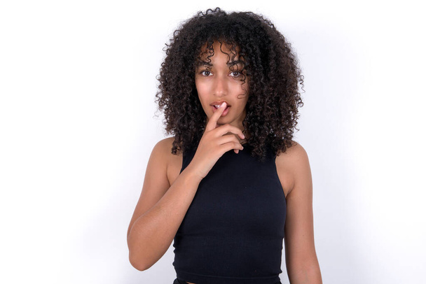Nervous puzzled Young African American woman wearing black T-shirt over white background opens mouth from surprise, reacts on sudden news. - 写真・画像