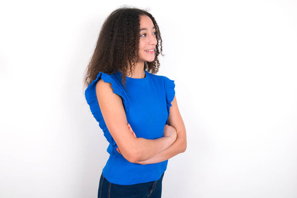 Дівчина-підліток з зачіскою на афро в синій футболці над білим тлом хрест руки дивіться копіювати простір
 - Фото, зображення