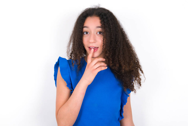 Nervoso confuso Adolescente com penteado afro vestindo camiseta azul sobre fundo branco abre boca de surpresa, reage em notícias repentinas. - Foto, Imagem