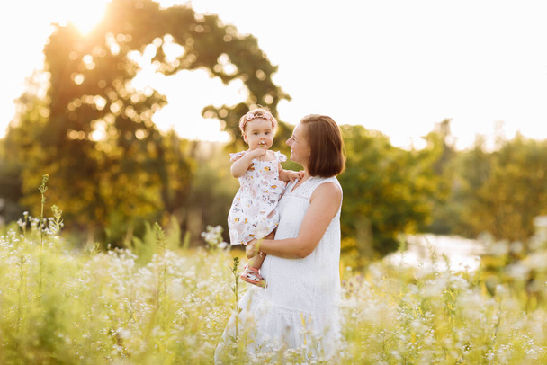 Щаслива молода мати грає зі своєю маленькою донькою в сонячний теплий весняний або літній день. Прекрасне світло на заході сонця в саду або в парку. Щаслива сімейна концепція
 - Фото, зображення