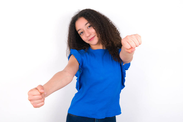 Adolescente chica con afro peinado usando azul camiseta sobre fondo blanco imaginar volante timón timón pasando examen de conducción buen humor velocidad rápida - Foto, imagen