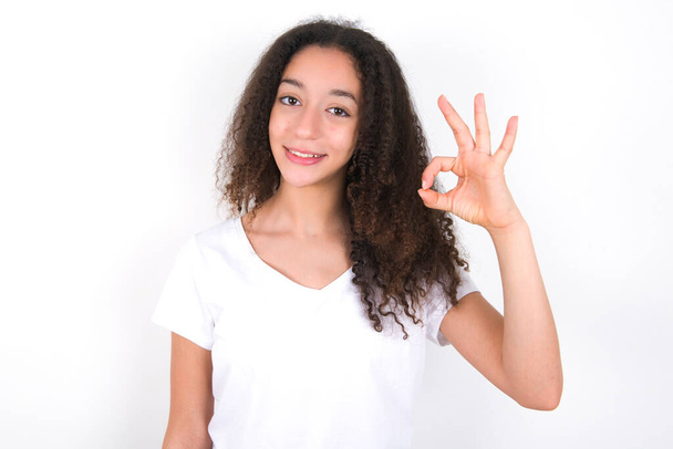 Дівчина-підліток з зачіскою на афро в білій футболці над білим тлом тримає руку джакузі символ зубного затвердження поради новинки
 - Фото, зображення