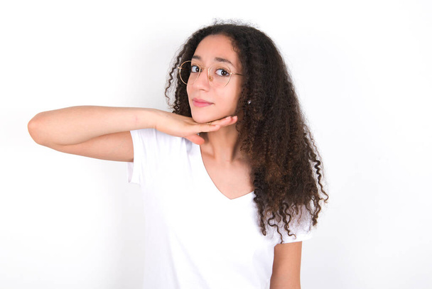 Дівчина-підліток з зачіскою на афро в білій футболці над білим тлом, що розрізає горло рукою як ніж, загрожує агресії з лютим насильством
. - Фото, зображення