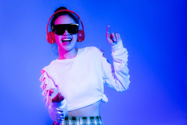 happy asian woman in white fashion crop sweatshirt wearing sunglasses and red headphones listen to music and dancing on purple color background. - Foto, imagen