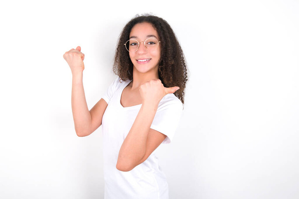 Hurrá hűvös tini lány afro frizura visel fehér póló felett fehér háttér pont vissza üres tér kéz ököl - Fotó, kép