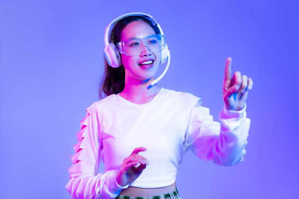 Young asian woman in white shirt wearing headphones posing finger pointing and touching on blue background. - Photo, Image
