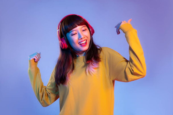Young asian woman in yellow sweatshirt wearing red headphones listen to music and dancing on the purple color background. - Foto, Imagen
