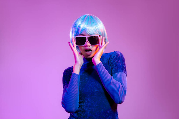 Young asian woman blue color short hair style in dark blue sweatshirt wearing sunglasses posing on purple background. - Фото, изображение