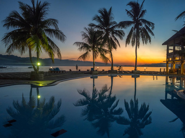 Kilátás sziluettjei pálmafák körül luxus medence alatt trópusi naplemente. Ambon-sziget. Indonézia - Fotó, kép
