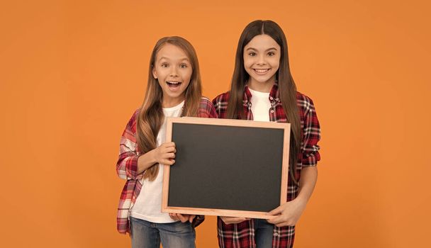 happy teen girls hold blackboard. children advertising. back to school. kids presenting novelty information. childhood education. copy space for announcement. educational offer promotion. school sale. - Photo, Image