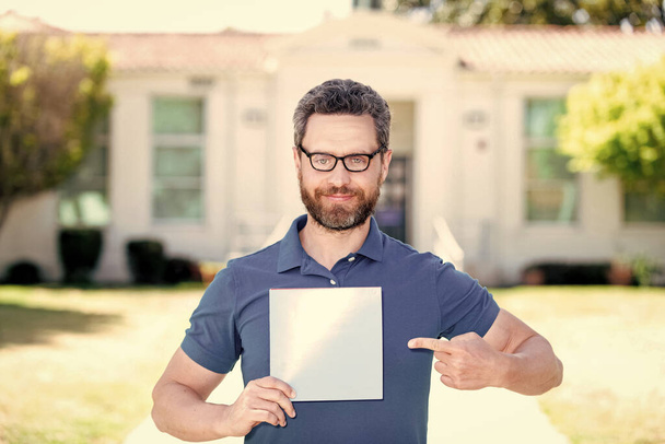 sonriente hombre nerd señalando dedo en hoja de papel presentando publicidad, espacio de copia, promoción. - Foto, Imagen