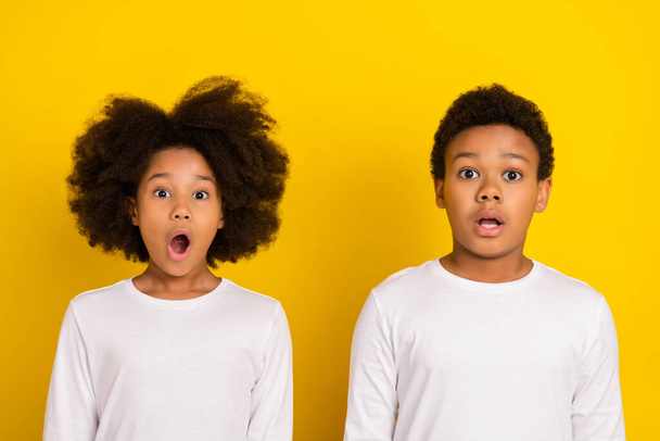 Photo of two impressed siblings open mouth stare speechless camera isolated on yellow color background. - Foto, Imagem