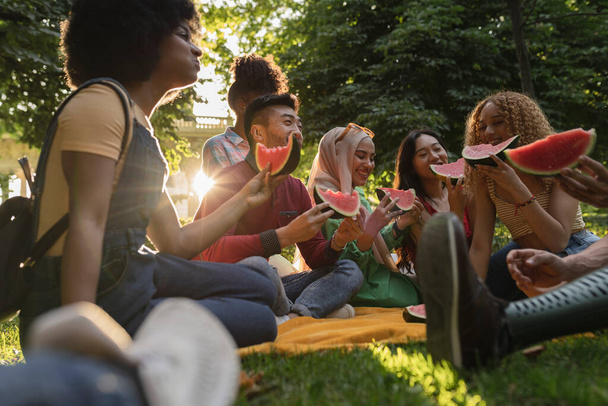 νέοι πολυ-εθνοτικοί φίλοι, απολαμβάνοντας το καλοκαίρι, στο πάρκο, στο ηλιοβασίλεμα, τη φιλία και το καλοκαίρι έννοια. - Φωτογραφία, εικόνα