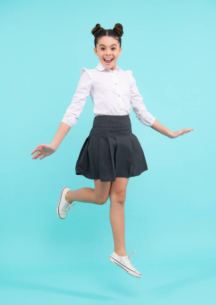 Happy funny excited jumping teenager. Happy schoolgirl, positive and smiling emotions of teen girl. Full length jump of teenager girl on blue isolated studio wear casual skirt and shirt - Zdjęcie, obraz