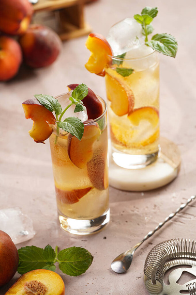 Two glasses with refreshing summer cocktail with ice cubes, peach slices and fresh mint on pale purple background - Photo, image