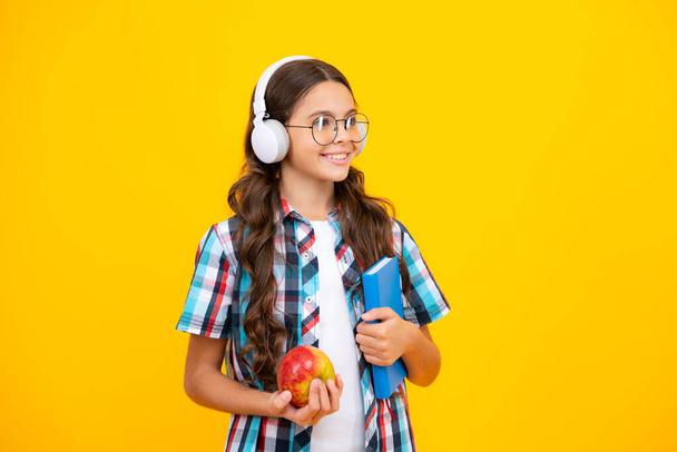 Back to school. Teenage school girl with bag hold apple and book, ready to learn. School children on isolated yellow background - Foto, imagen