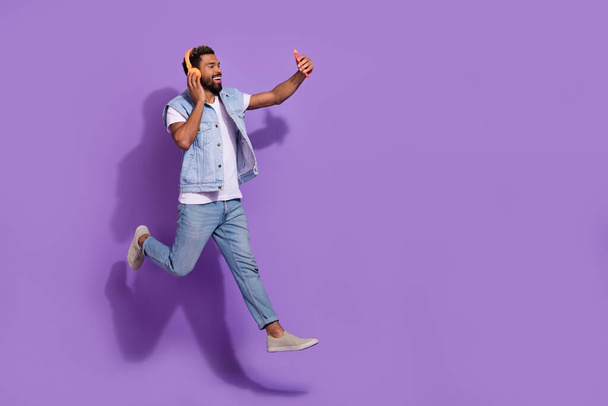 Full length photo of cheerful positive man wear jeans jumping empty space recording self video isolated violet color background. - Valokuva, kuva