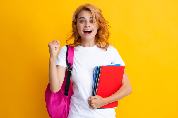 Cute student woman with backpack holds some documents and books over yellow background. Portrait of smiling young woman student in shirt backpack hold notebooks. Education in high school university - Photo, Image