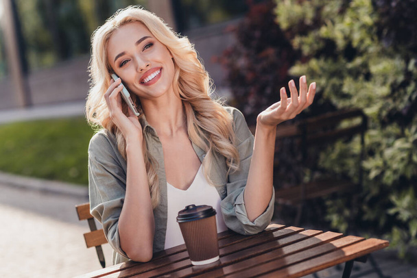 Portrait of attractive cheerful wavy haired girl talking on phone spending time day drinking coffee latte rest relax outside. - Zdjęcie, obraz