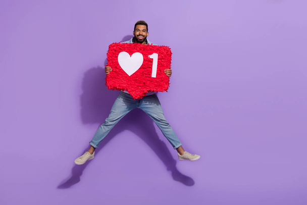 Full length photo of pretty positive man wear jeans jumping empty space holding like pinata isolated violet color background. - Foto, afbeelding