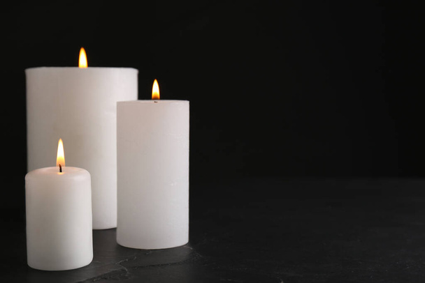 Burning candles on slate table against black background. Space for text - Photo, Image