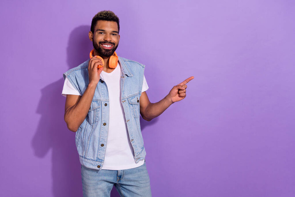 Photo of cute funky man wear jeans waistcoat headphones pointing finger empty space isolated violet color background. - Fotó, kép