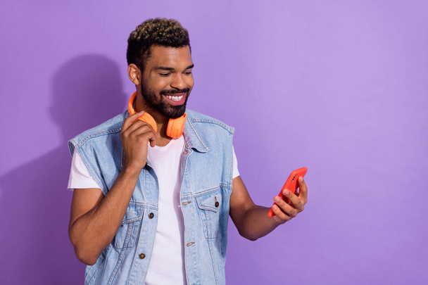 Photo of cheerful cute man wear jeans waistcoat headphones listening player modern gadget empty space isolated violet color background. - 写真・画像