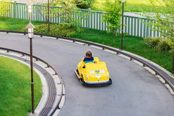 Een kleine jongen rijdt in een miniatuur gele auto op de weg in de kinderstad. Racebaan voor kinderen in het pretpark - Foto, afbeelding