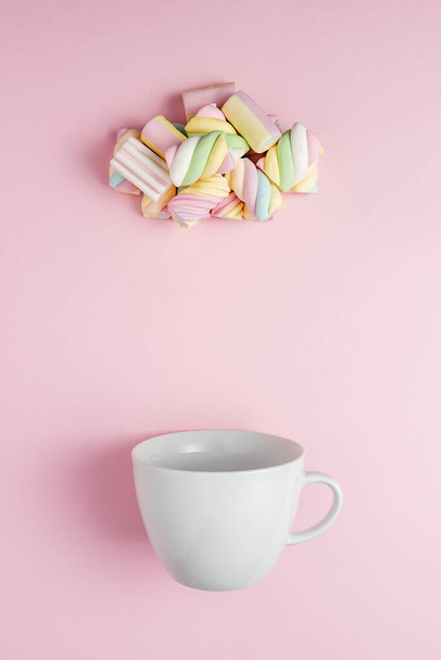Marshmallows in shape of rainy cloud with white cup on pink background. Creative minimal sweet holiday food concept. - Photo, image
