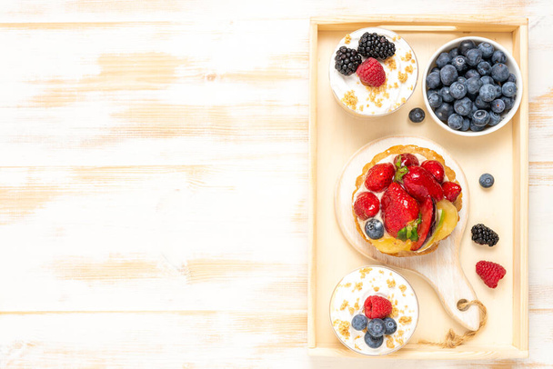 Sweet desserts with fresh berries on wooden background. - Photo, image