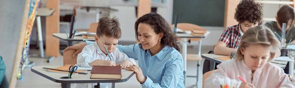 Happy kind leraar is het helpen van kinderen in de lagere school lessen. - Foto, afbeelding