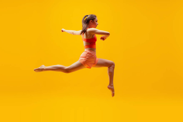 In motion, energy. Full-length portrait of young slim girl running isolated on bright yellow background. Modern sport, action, motion, summer, vacation, youth concept. - Valokuva, kuva