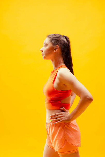 Looks calm. Profile view of young girl wearing summer sports style outfit isolated on bright yellow background. Modern sport, action, motion, summer, vacation, youth concept. - Foto, afbeelding
