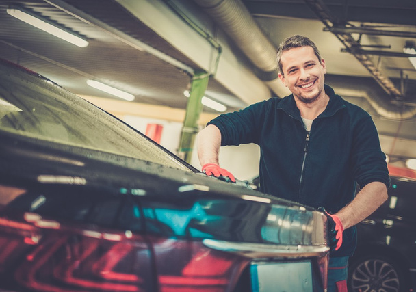 Trabajador alegre limpiando el coche en un lavado de coches
 - Foto, Imagen