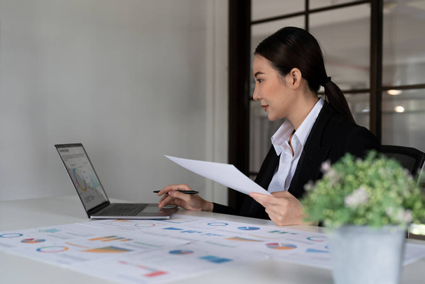 Portrait of Young Successful Asian Businesswoman Sitting at Desk Working on Laptop Computer in Office. Ambitious Corporate Manager Plan Investment Strategy for e-Commerce Project - 写真・画像