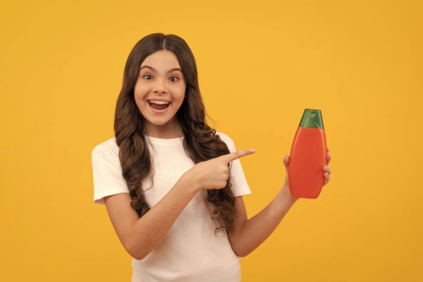 fille adolescente étonnée avec les cheveux longs pointant doigt sur bouteille de shampooing, promotion. - Photo, image