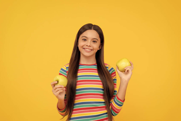 Ευτυχισμένο κορίτσι παιδί κρατήσει τα μήλα κίτρινο φόντο, διατροφή των παιδιών. - Φωτογραφία, εικόνα