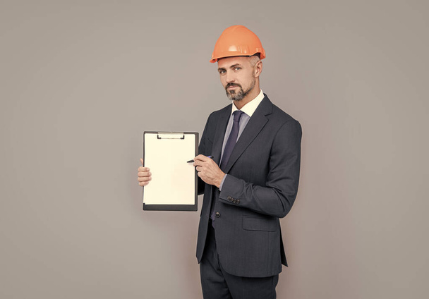 architect man in businesslike suit and hardhat showing clipboard, copy space, result. - Foto, afbeelding