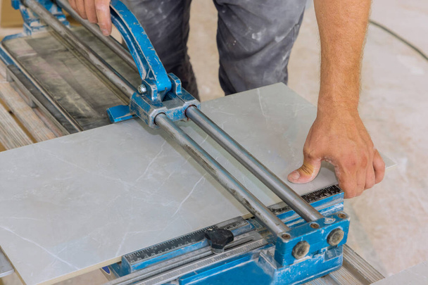 Rakennustyöntekijä leikkaa keraamiset laatta lattiapinnat käsityökaluja ja laitteita, jotta antaa keraamiset laatat lattialle. - Valokuva, kuva