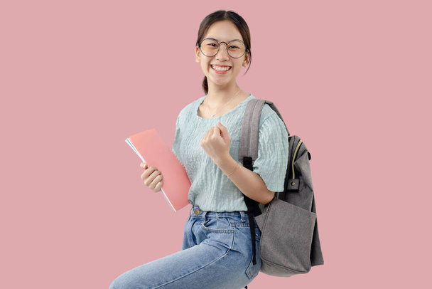 Счастливая молодая азиатская студентка стоит на изолированном розовом фоне. - Фото, изображение
