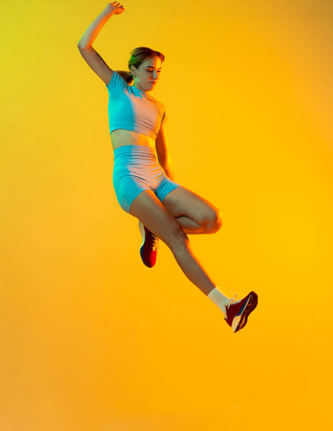 High jump. Professional longjumper. One female athlete in sports uniform jumping isolated on yellow background. Concept of sport, action, motion, speed, healthy lifestyle. Copy space for ad - Fotoğraf, Görsel