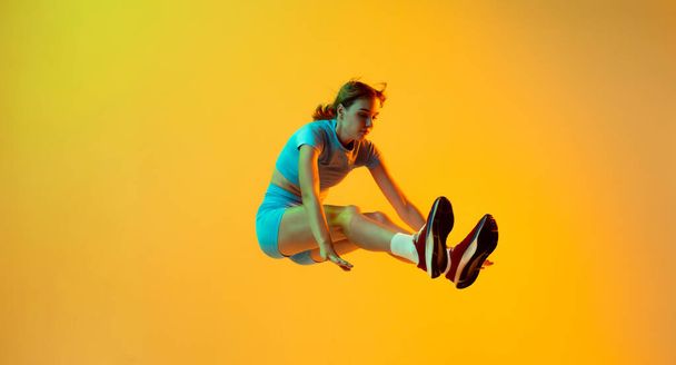 Flying. Professional longjumper. One female athlete in sports uniform jumping isolated on yellow background. Concept of sport, action, motion, speed, healthy lifestyle. Copy space for ad - Photo, image