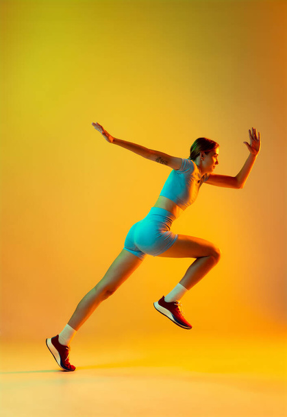 Runner. Professional longjumper. One female athlete in sports uniform jumping isolated on yellow background. Concept of sport, action, motion, speed, healthy lifestyle. Copy space for ad - Foto, imagen