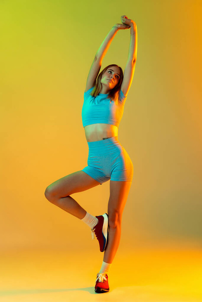 Portrait of young beautiful sportive girl in sports uniform posing isolated on yellow background. Concept of sport, action, motion, speed, healthy lifestyle. Copy space for ad - Zdjęcie, obraz